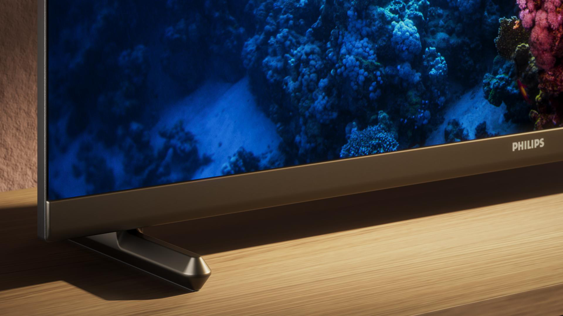 Fernseher mit blauem Korallenbild und braunem Sockel. Der Fernseher steht auf Holz.