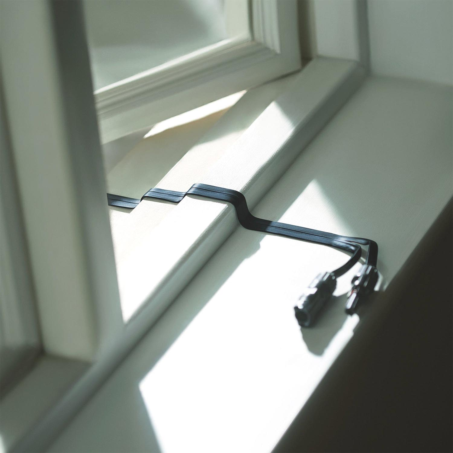 Ein Fenster mit einem schwarzen Kabel auf der Fensterbank. Sonnenlicht scheint.