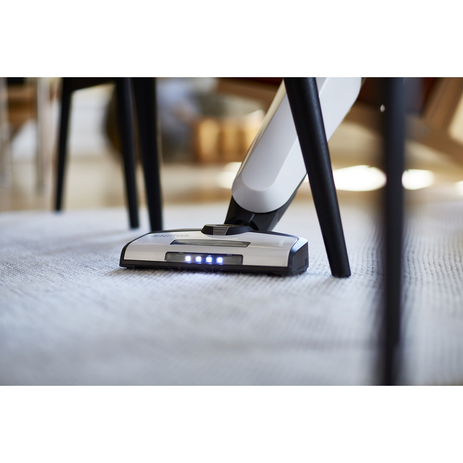 Tête d'aspirateur sur tapis, pieds noirs en arrière-plan.
