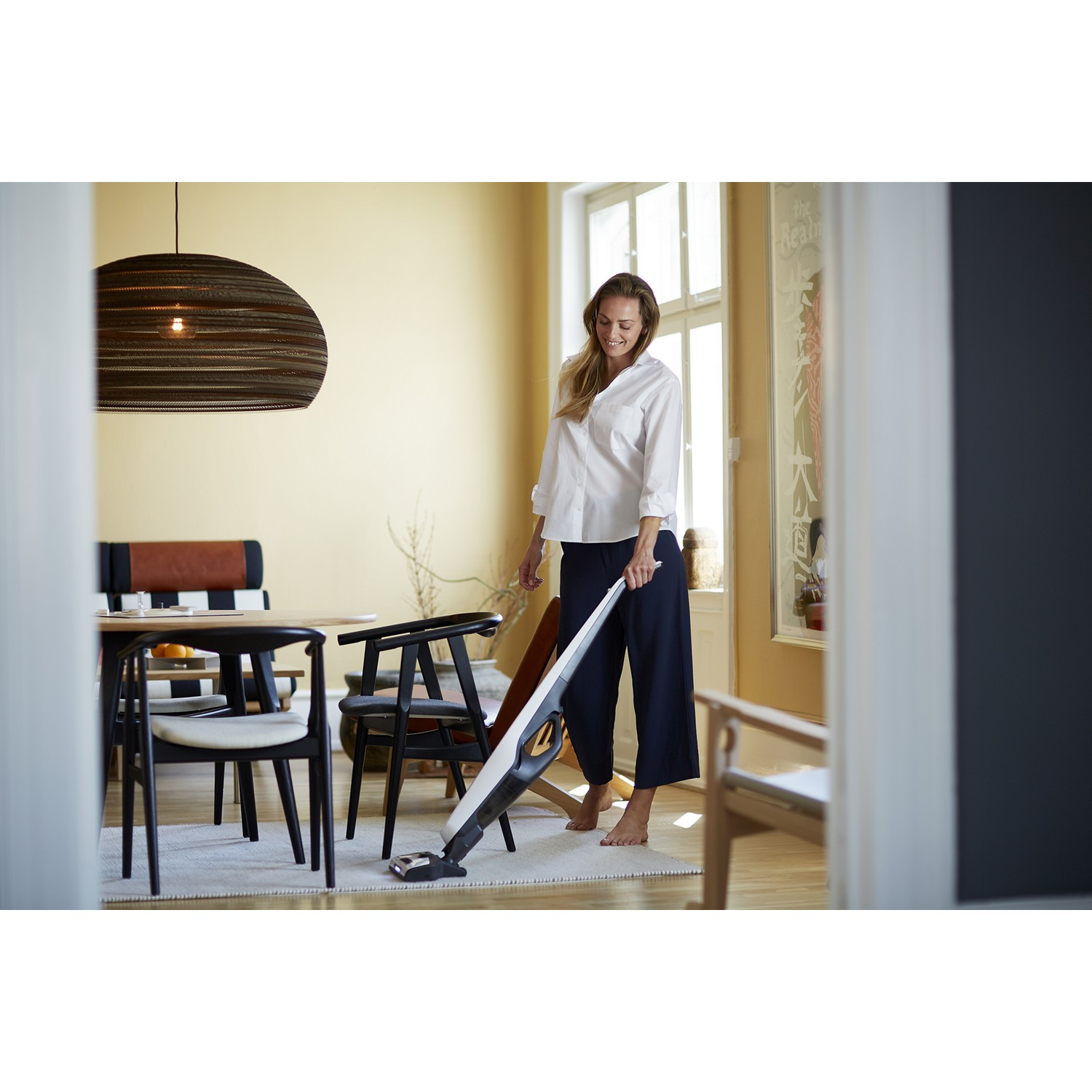 Femme passant l'aspirateur dans une pièce avec un aspirateur blanc et noir, près d'une table et des chaises.