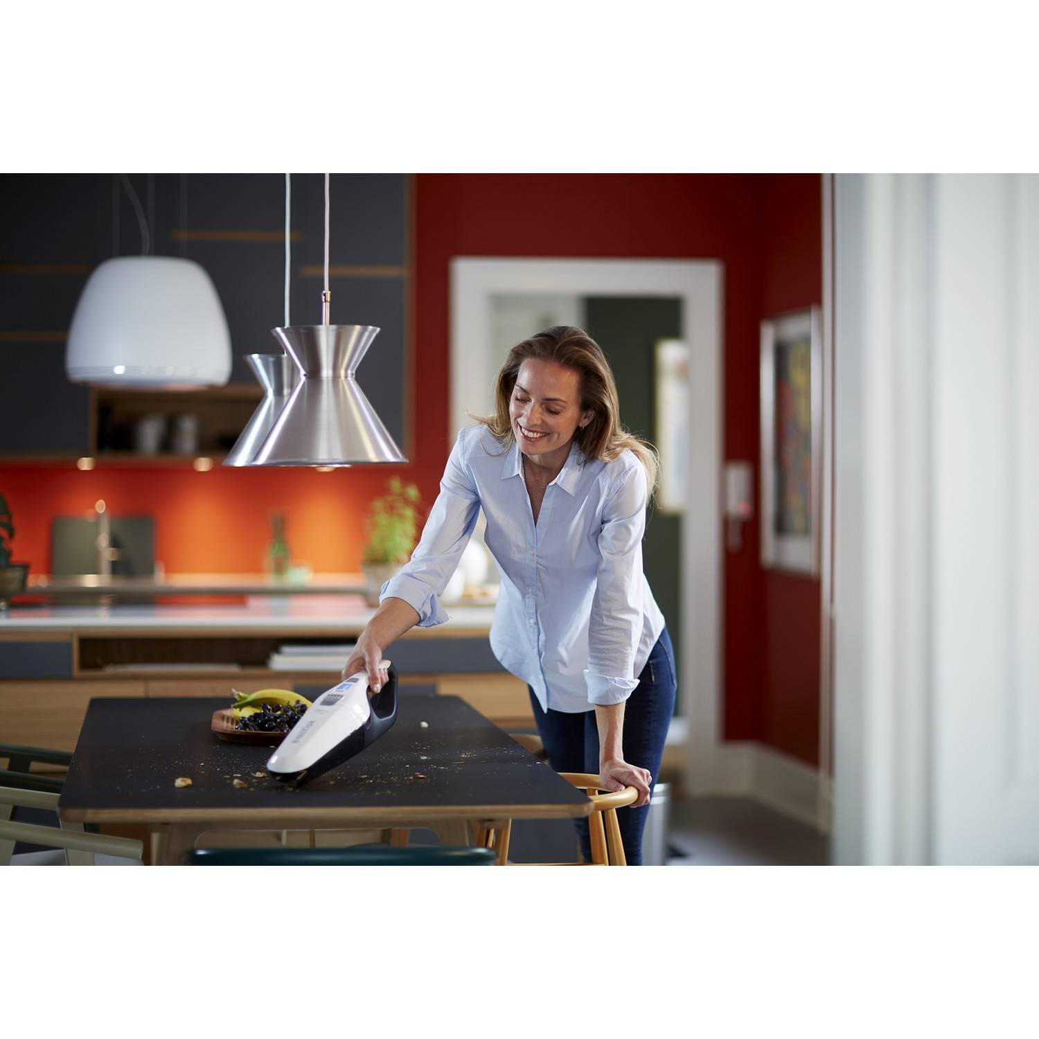 Femme passant l'aspirateur sur une table avec un aspirateur à main dans une cuisine. Mur rouge.