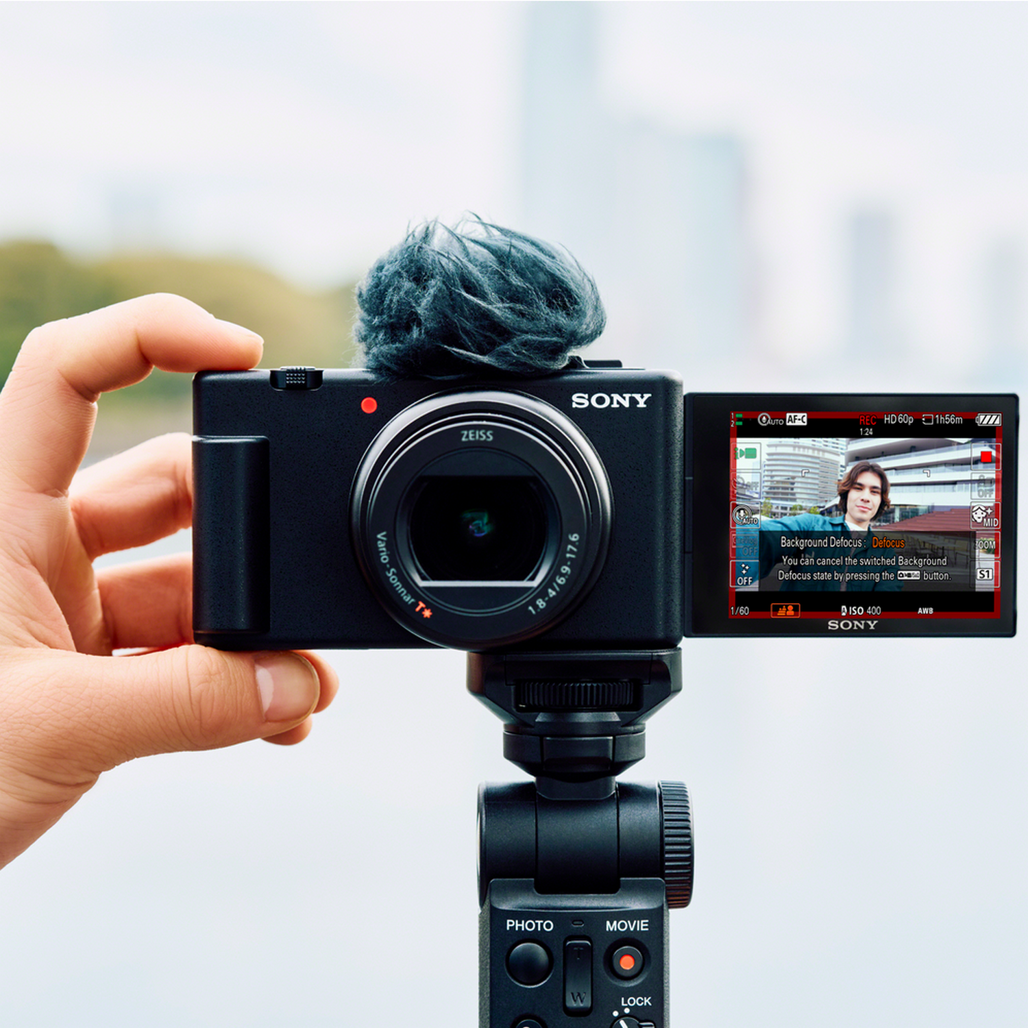 A black Sony camera with a microphone on a tripod, held by a hand, showing a video.