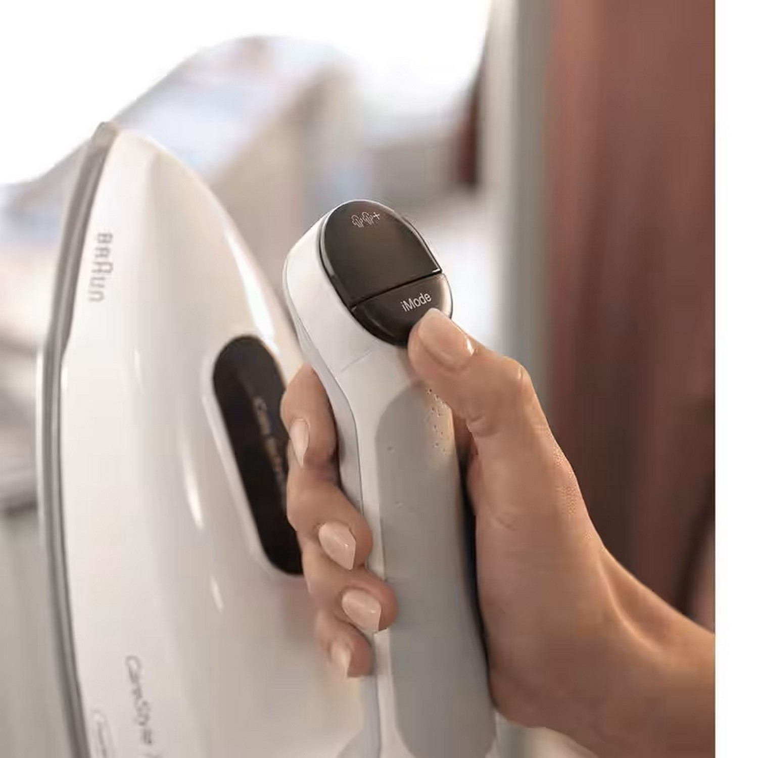 A woman's hand holding a white iron with a black control panel.
