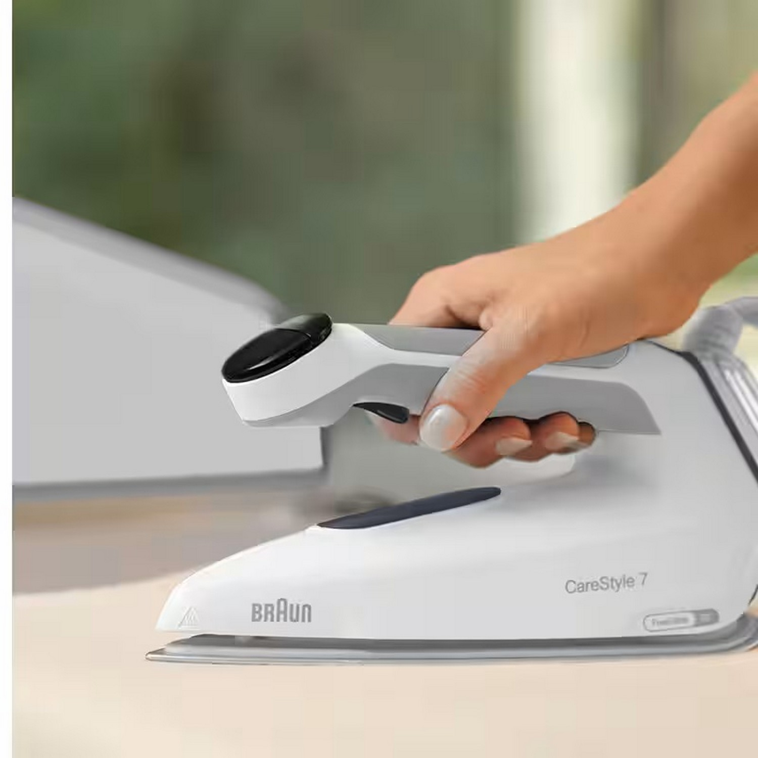 A white iron with a gray handle is held by a person's hand. Another iron is in the background.