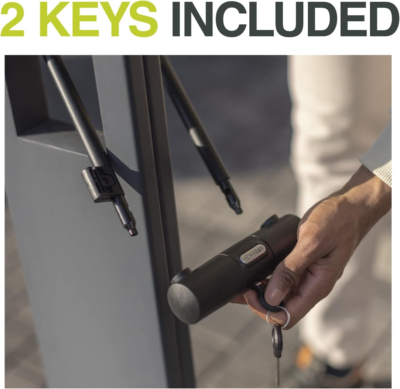 Die Hand einer Person, die einen Schlüssel hält, mit einem schwarzen U-Schloss und dem Text '2 KEYS INCLUDED'.