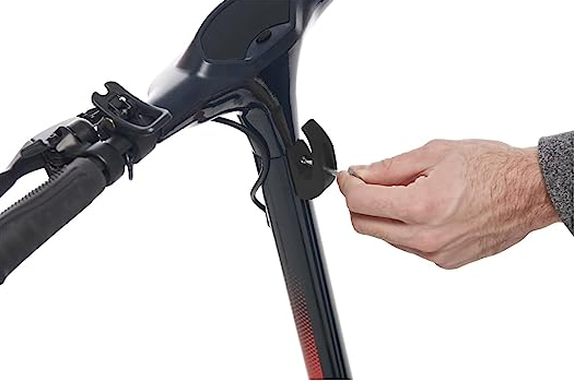 La mano di una persona avvita un pezzo al manubrio nero di uno scooter. Lo sfondo è bianco.
