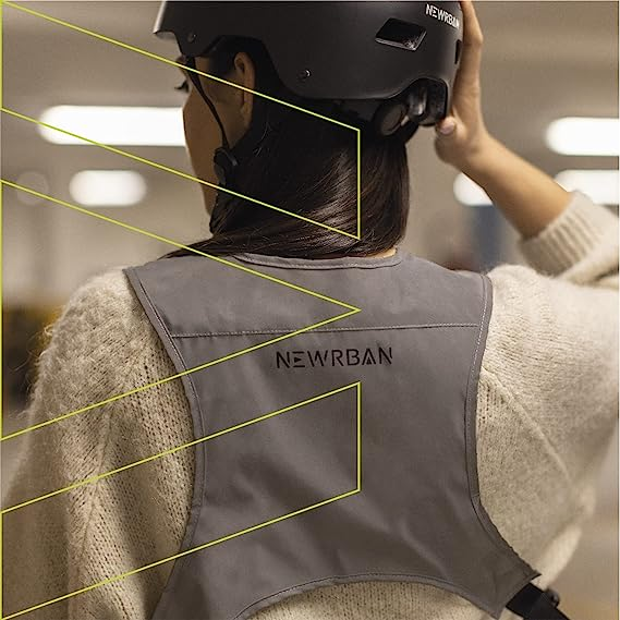 Personne portant un gilet réfléchissant gris avec 'NEWRBAN' dans le dos, dans un bâtiment.