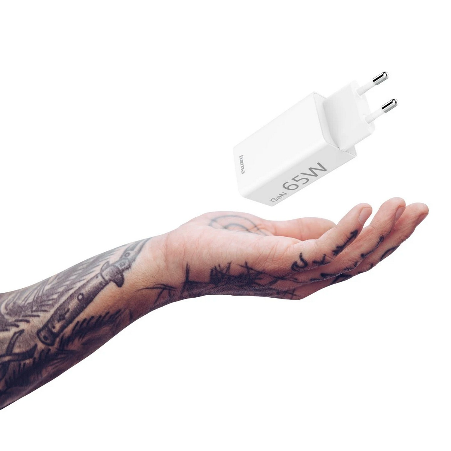 Un chargeur blanc Hama GaN 65W plane au-dessus d'une main tatouée. Il a deux broches et un design simple.