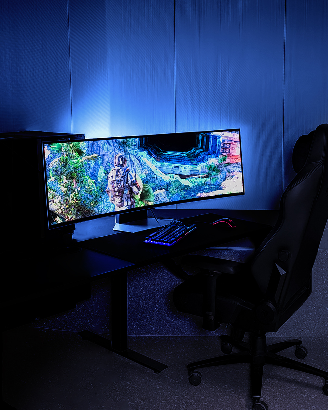 Gaming-Setup mit gebogenem Monitor, Tastatur, Maus und Stuhl in blauem Raum.