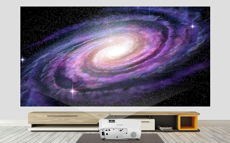 Projektor na stojaku, wyświetlający galaktykę na ścianie.