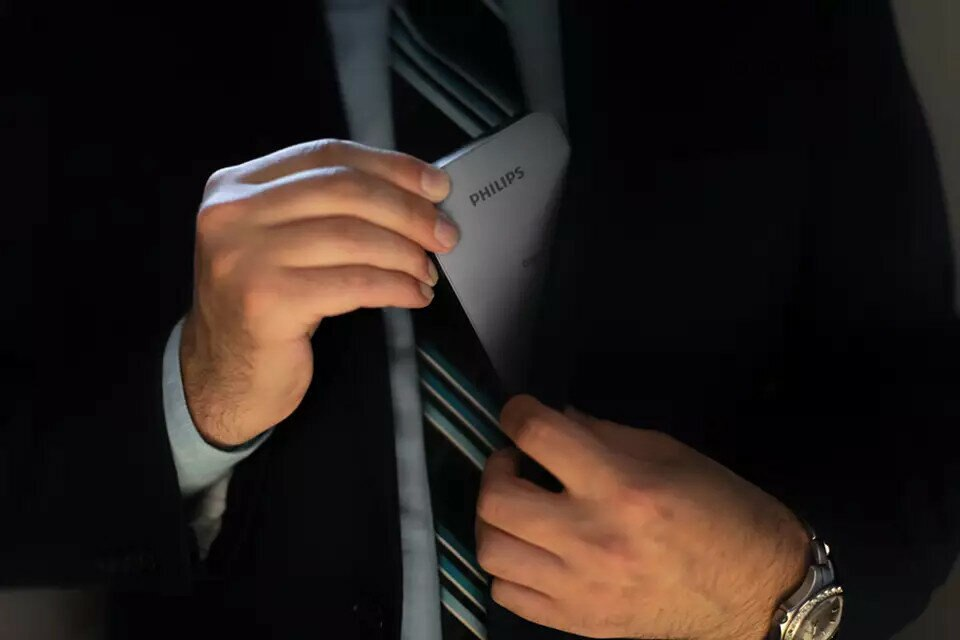 Mężczyzna w garniturze wkłada do kieszeni szare, prostokątne urządzenie z logo Philips.