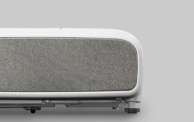 Zbliżenie białego projektora, pokazujące głośnik pokryty siatką na jasnoszarym tle.