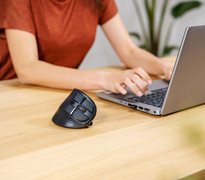 Nő laptopon dolgozik, függőleges egérrel egy fa asztalon.
