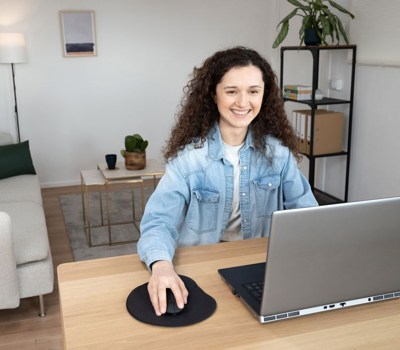 Nő laptopon dolgozik egy fa asztalon, egérrel és egy növénnyel.