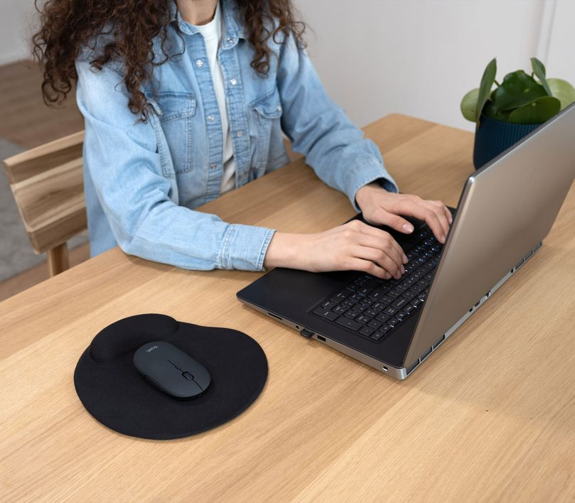 Egy nő laptopot használ, egérrel és egérpaddal az asztalon.