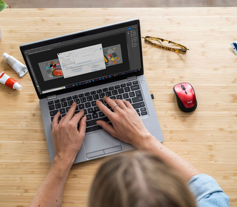 Személy laptopot használ piros egérrel az asztalon.