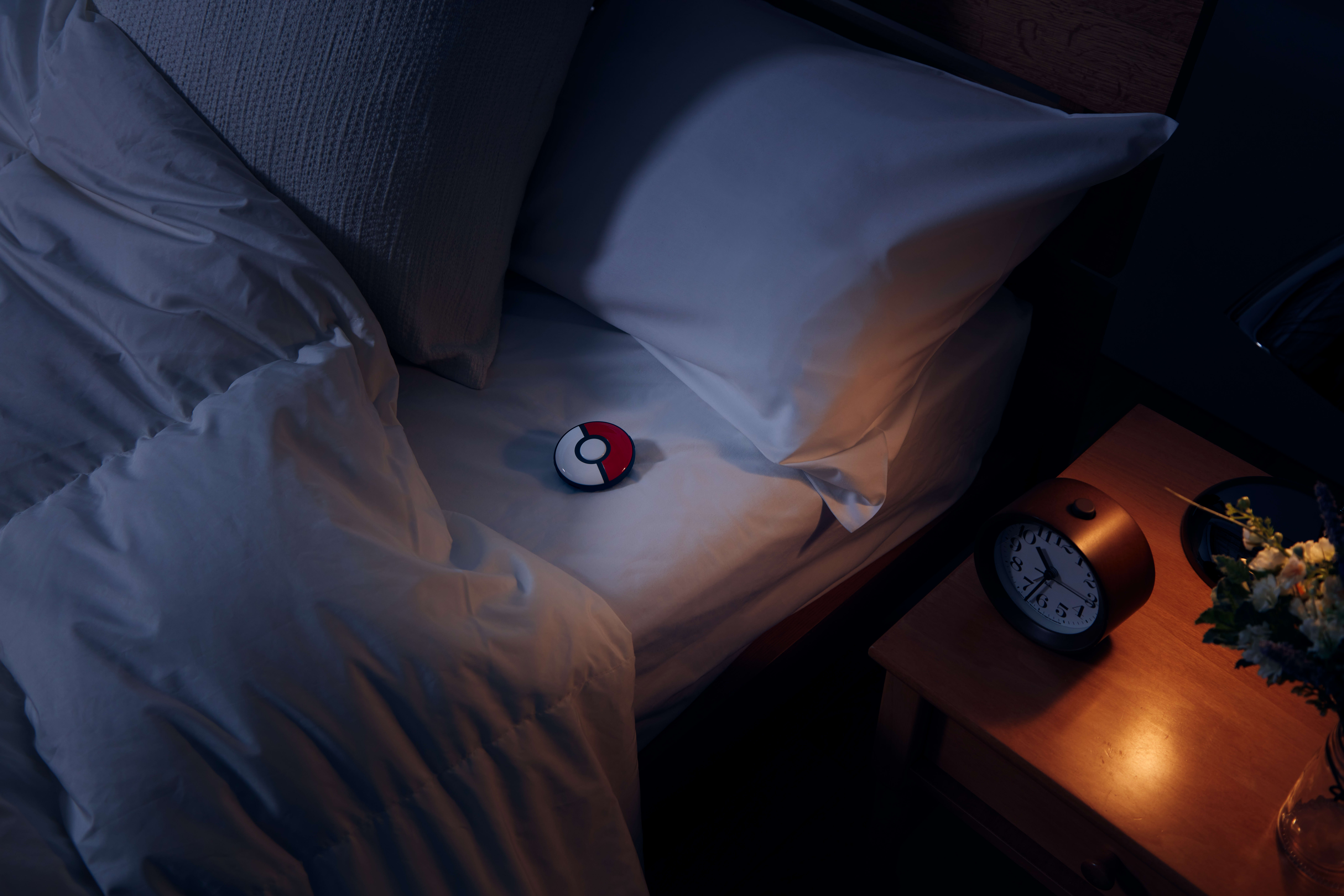Ein Bett mit weißem Kissen und einem Pokemon Go Plus-Gerät auf dem Bett.