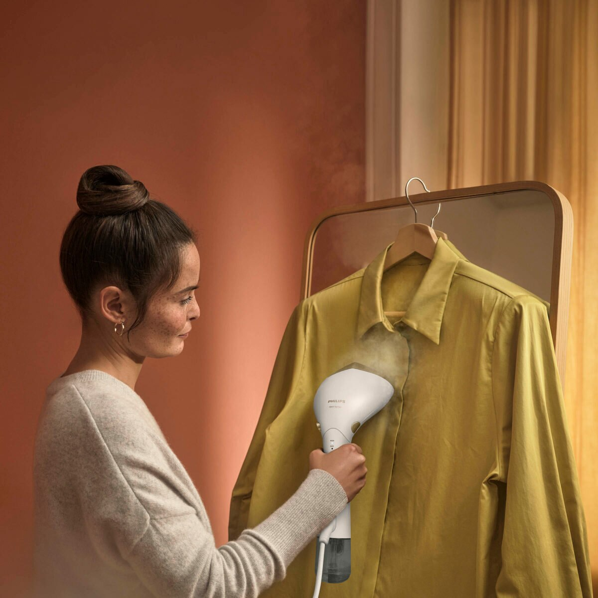 Kobieta prasująca żółtą koszulę na wieszaku za pomocą parownicy Philips.