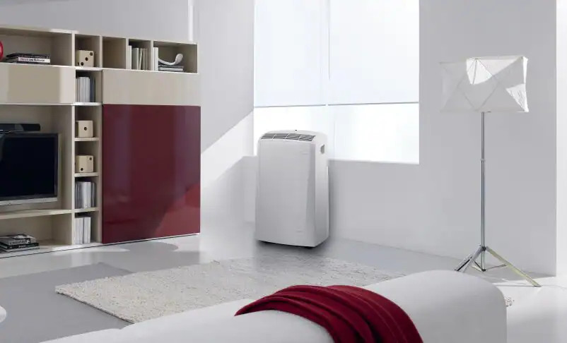 Woonkamer met witte muren, een witte bank, een rode deken en een airconditioner.