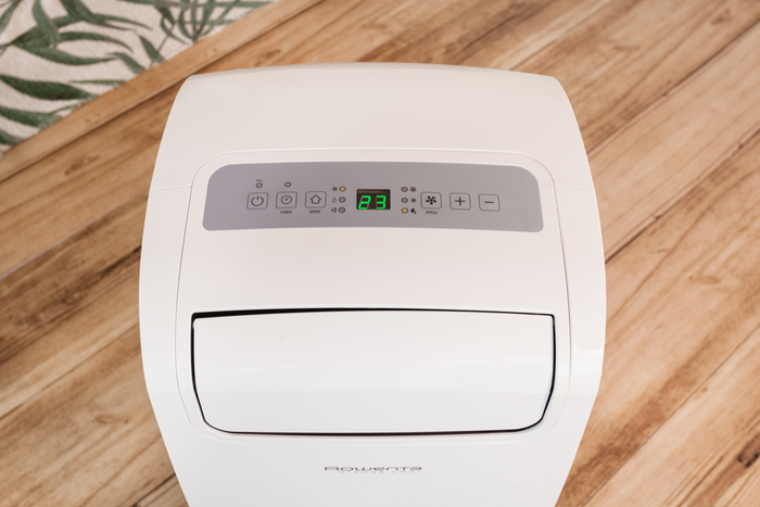 Witte Rowenta draagbare airconditioner met een bedieningspaneel en temperatuurweergave. Houten vloer.