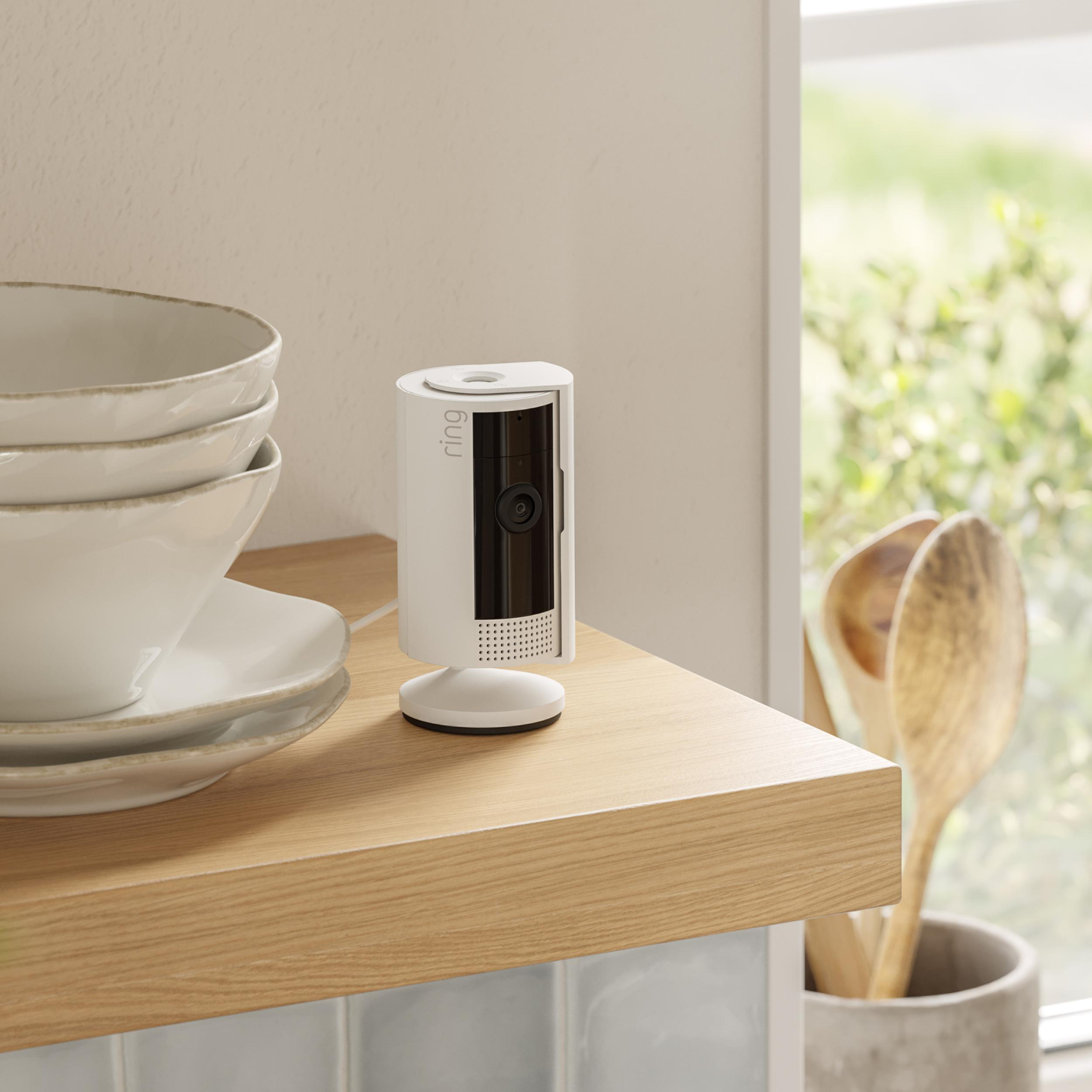 Eine weiße Ring-Kamera auf einem Holzregal mit Schüsseln und Kochutensilien.