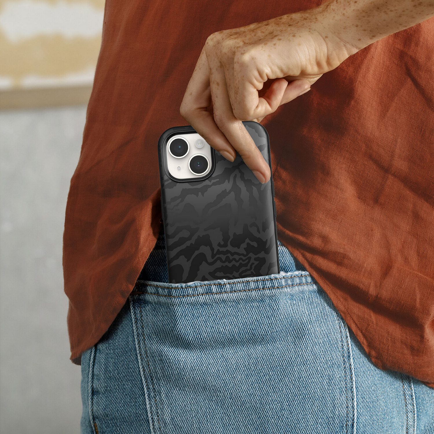 De hand van een persoon die een zwart telefoon met patroon in een zak van een spijkerbroek steekt.