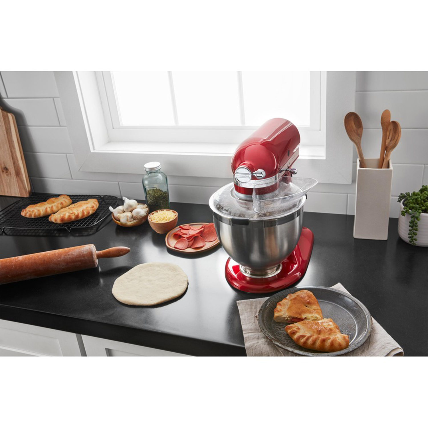 Impastatrice KitchenAid rossa con ingredienti per pizza, su un piano di lavoro nero.