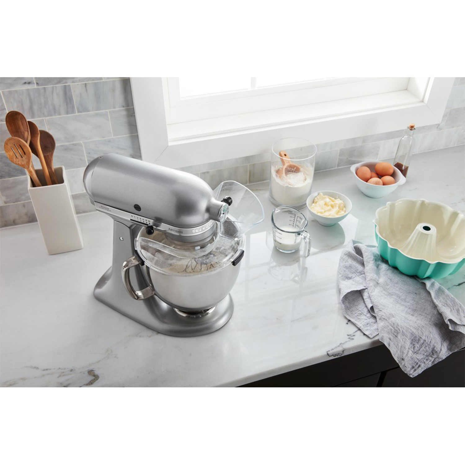 Un mixer KitchenAid argentato che mescola gli ingredienti con utensili e ingredienti da cucina.
