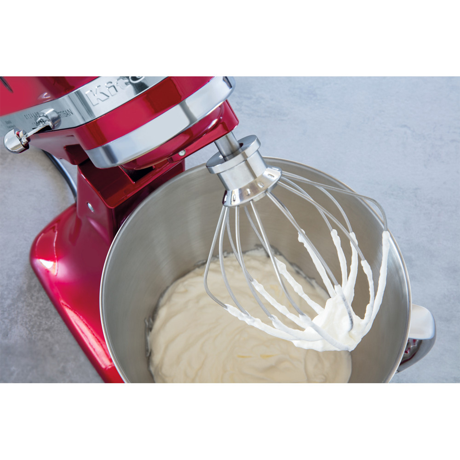 Frullatore KitchenAid rosso con frusta che mescola panna bianca in una ciotola in acciaio inox.