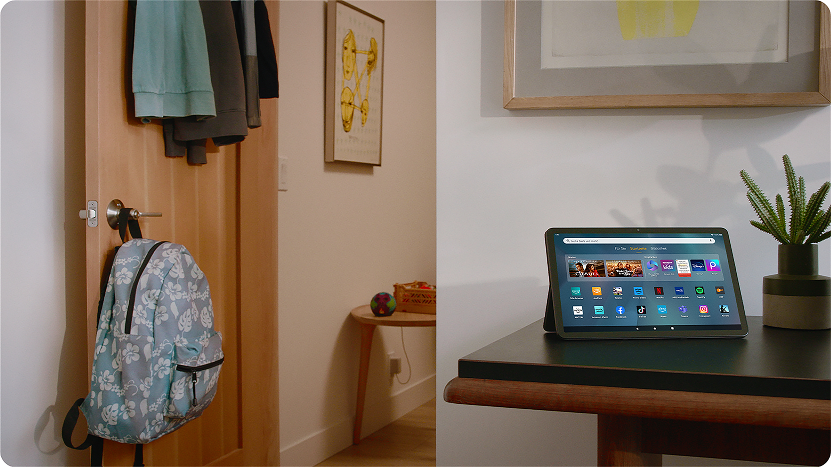 Tablet auf einem Tisch mit Tür und Rucksack im Hintergrund. Kunstwerk an der Wand.