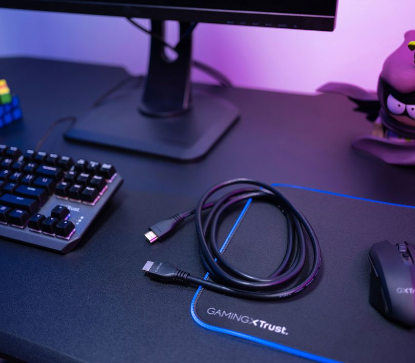 Egy asztal billentyűzettel, egérrel, HDMI kábellel és monitorral. Fekete asztal. Közeli kép.