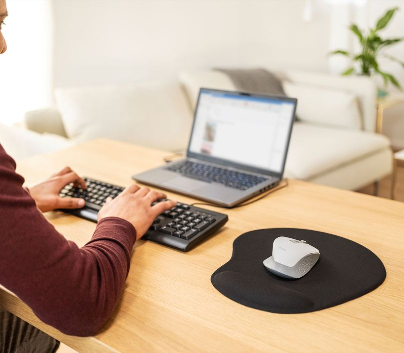 Egy személy laptopon dolgozik, billentyűzettel és egérrel egy fa asztalon.