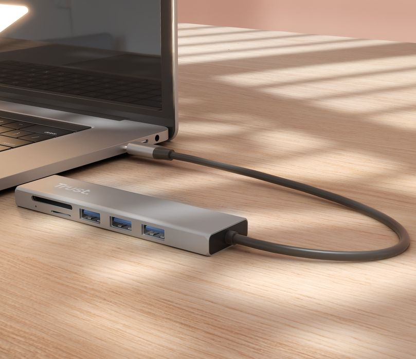 Ezüst USB hub laptophoz csatlakoztatva. SD kártyanyílás és USB portok láthatók. Fa asztal háttér.