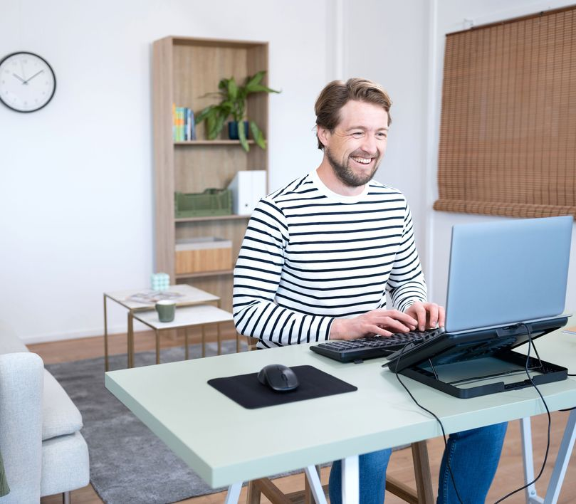 Egy férfi egy laptopon dolgozik egy asztalnál egérrel, mosolyogva.