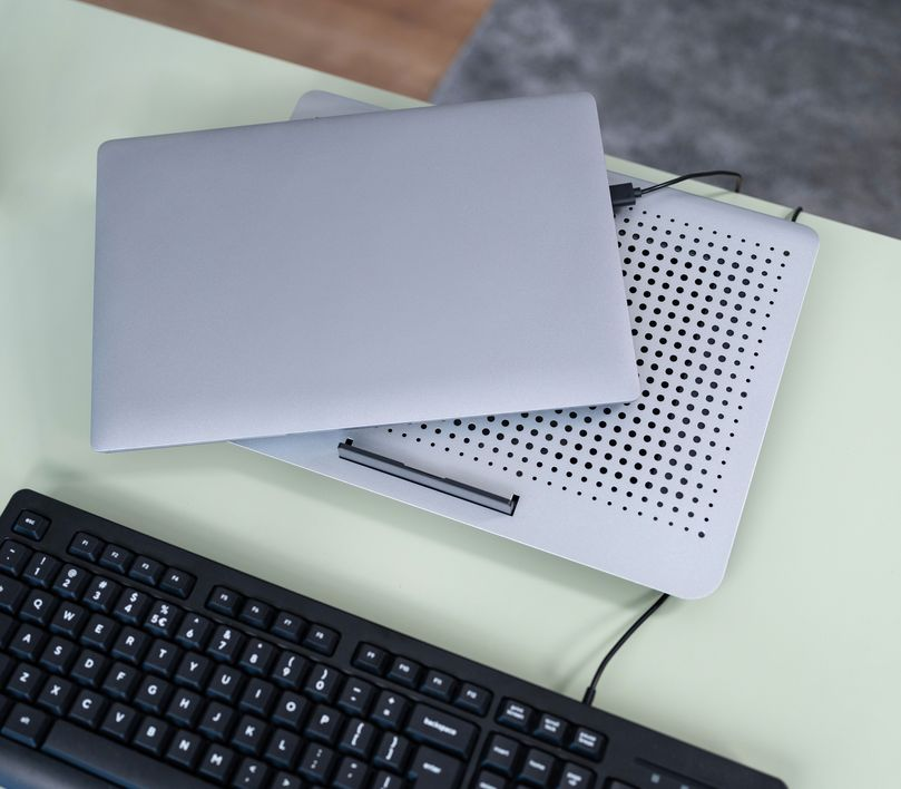 Egy szürke laptop egy hűtőpulton, egy billentyűzettel egy világoszöld asztalon.
