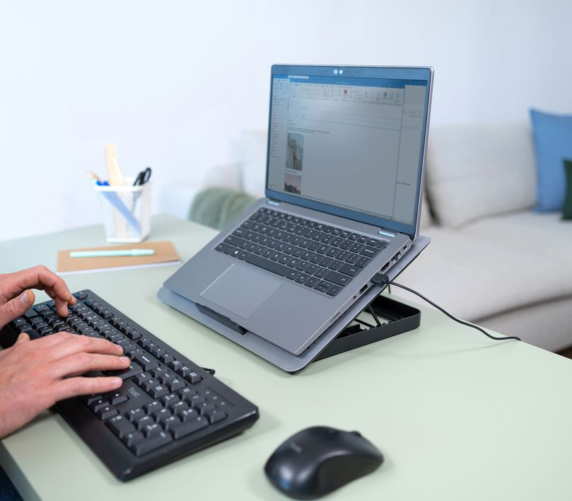 Egy személy, aki billentyűzeten gépel, laptop a tartón, egér az asztalon.