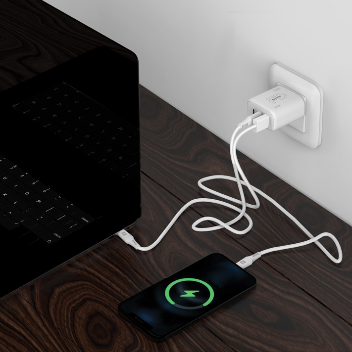 Telefon, das in der Nähe eines Laptops geladen wird. Weißes Ladegerät und Kabel. Telefon zeigt Ladesymbol.