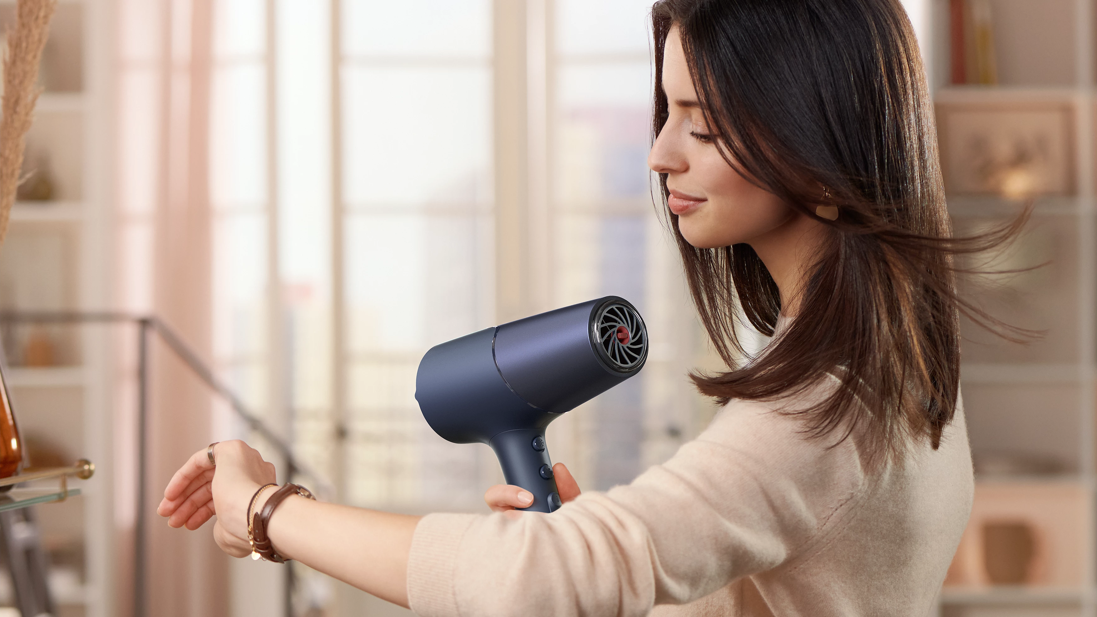 Frau trocknet Haare mit blauem Haartrockner, Profilansicht, in hellem Raum.