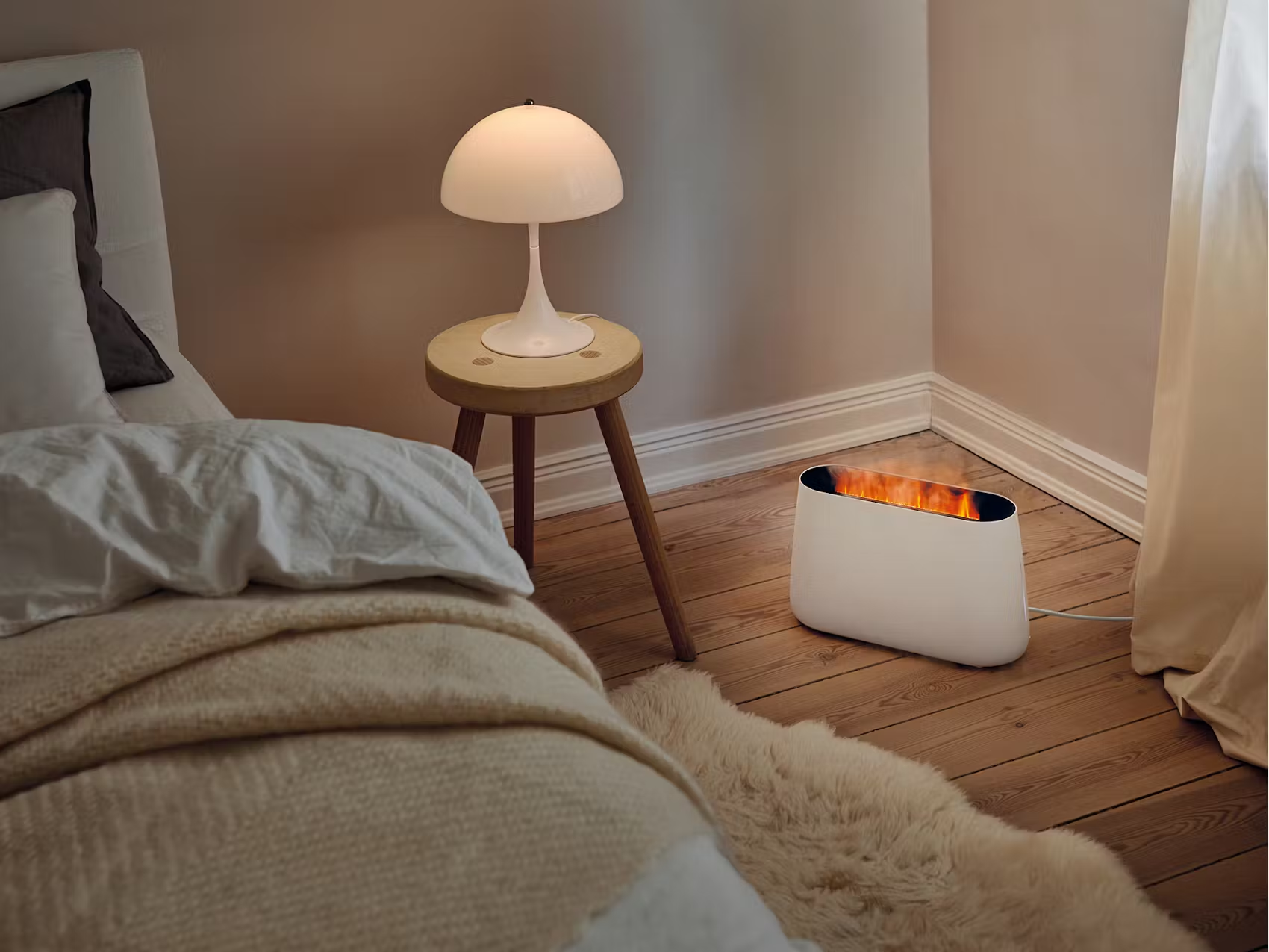 Scena di camera da letto con un termoconvettore bianco effetto fuoco, una lampada e un letto. Pavimento in legno.