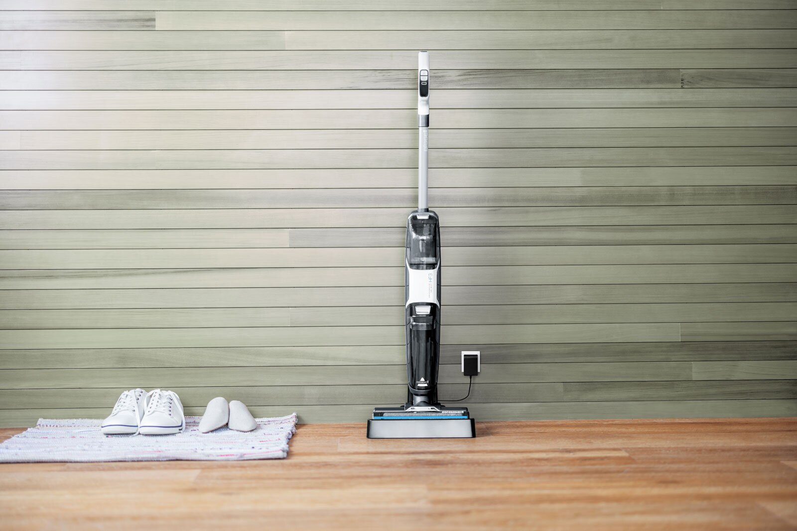 Biało-czyszczący do podłóg na tle ściany z drewnianymi panelami. W pobliżu buty i mata.