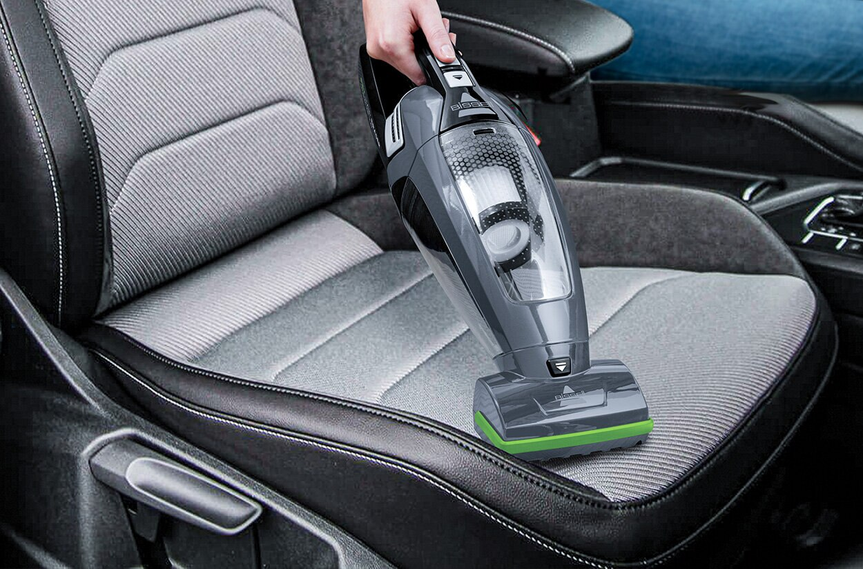 Ręczne odkurzanie siedzenia samochodowego odkurzaczem ręcznym, szarym i czarnym z zielonymi akcentami.