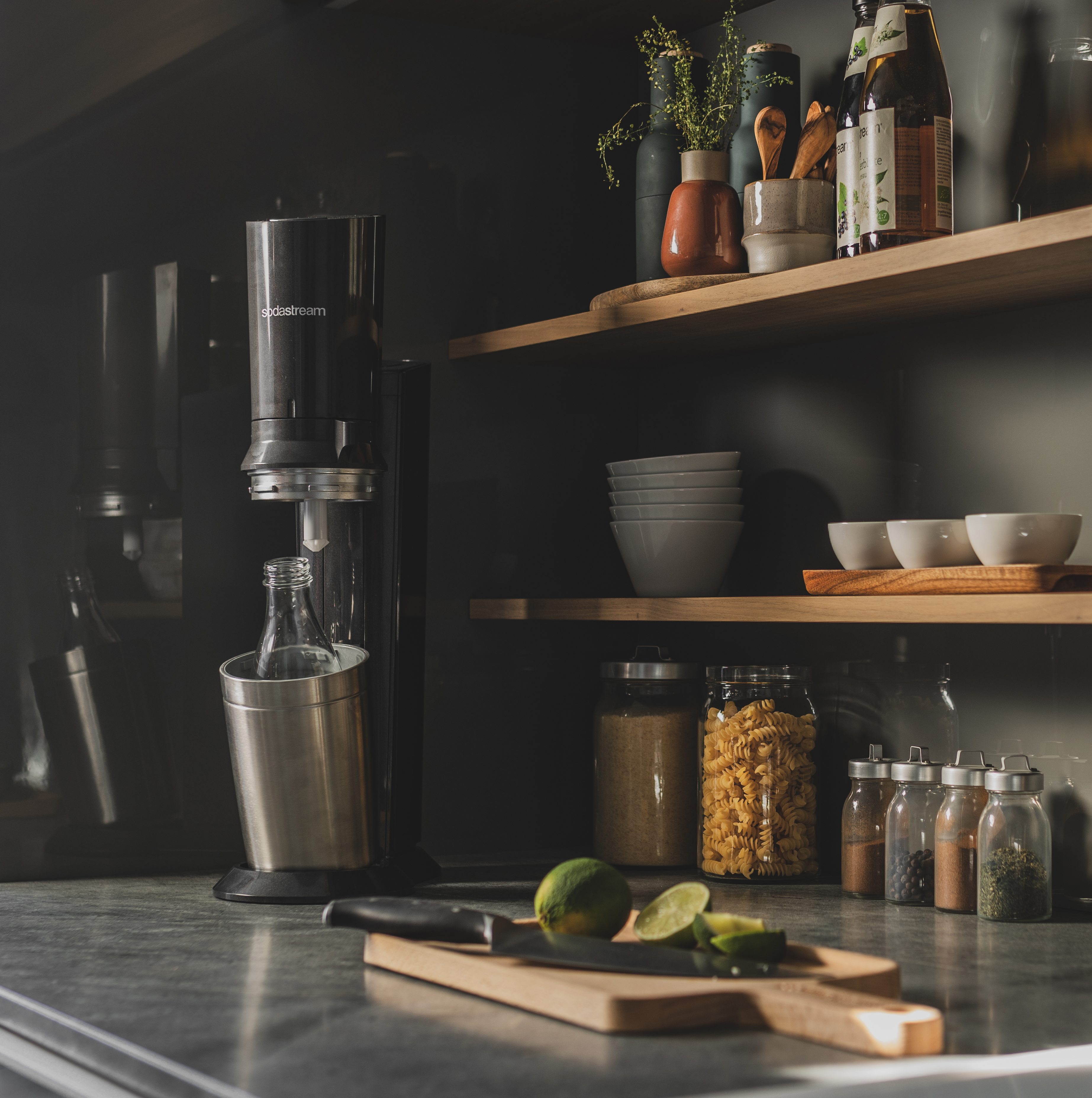 Scène de cuisine : Machine à soda, ingrédients, planche à découper avec citron vert et couteau.