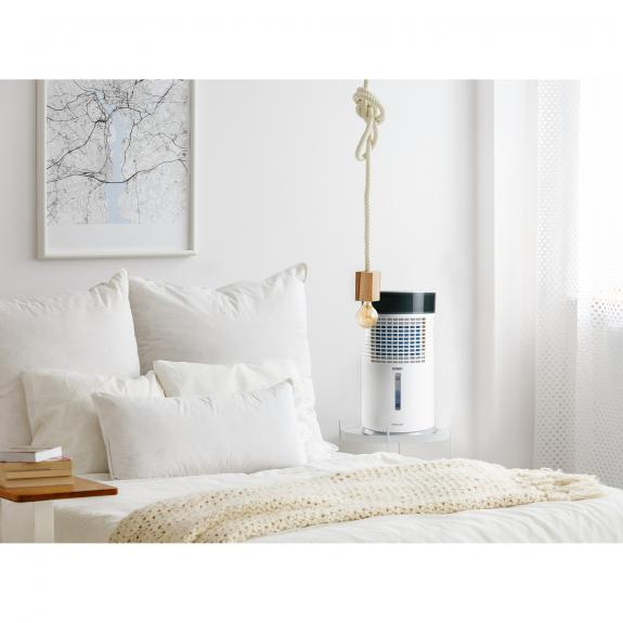 Chambre blanche avec lit blanc, oreillers et un refroidisseur d'air suspendu.