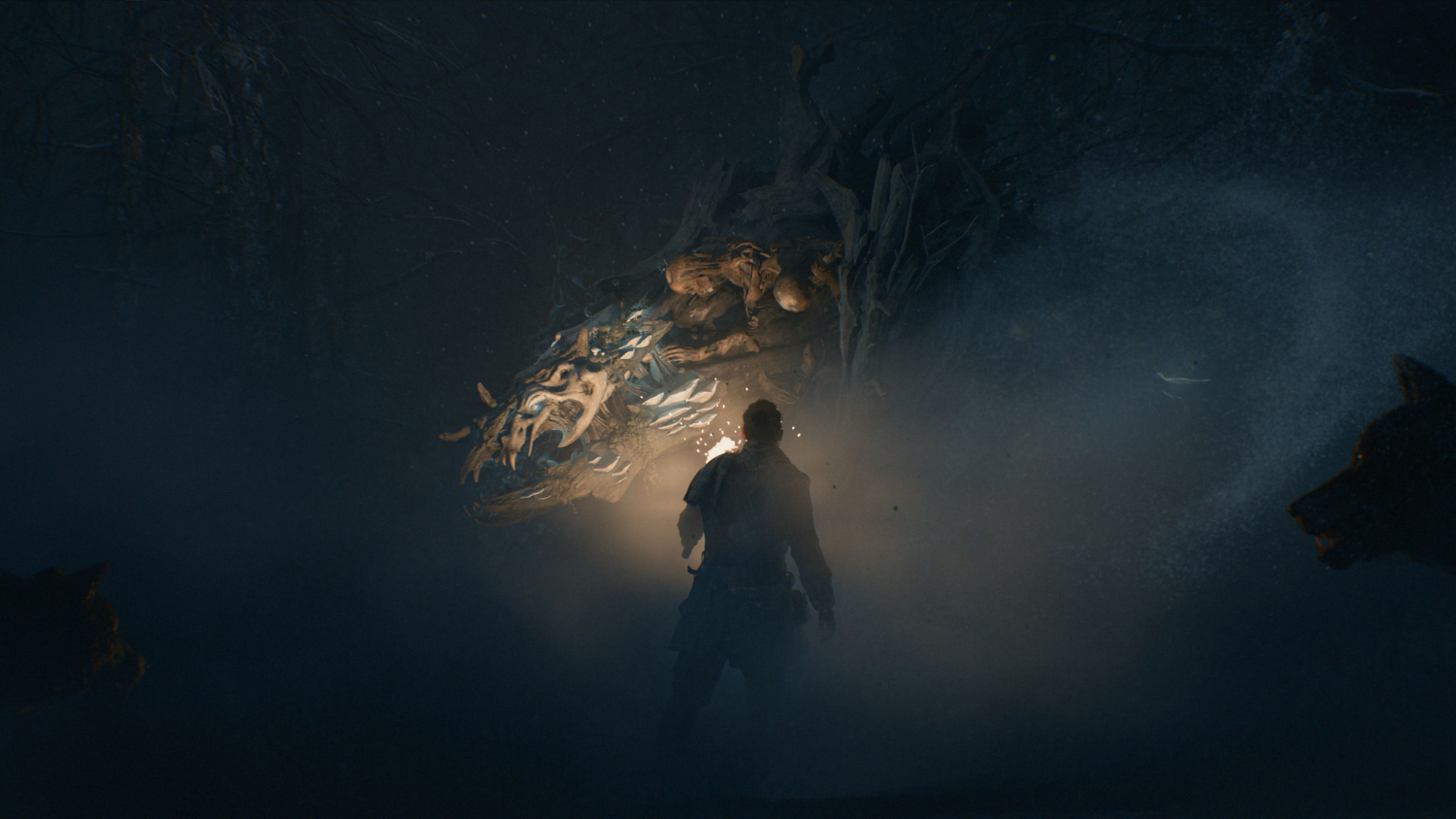 Une figure avec une torche dans une grotte sombre, face à une statue.