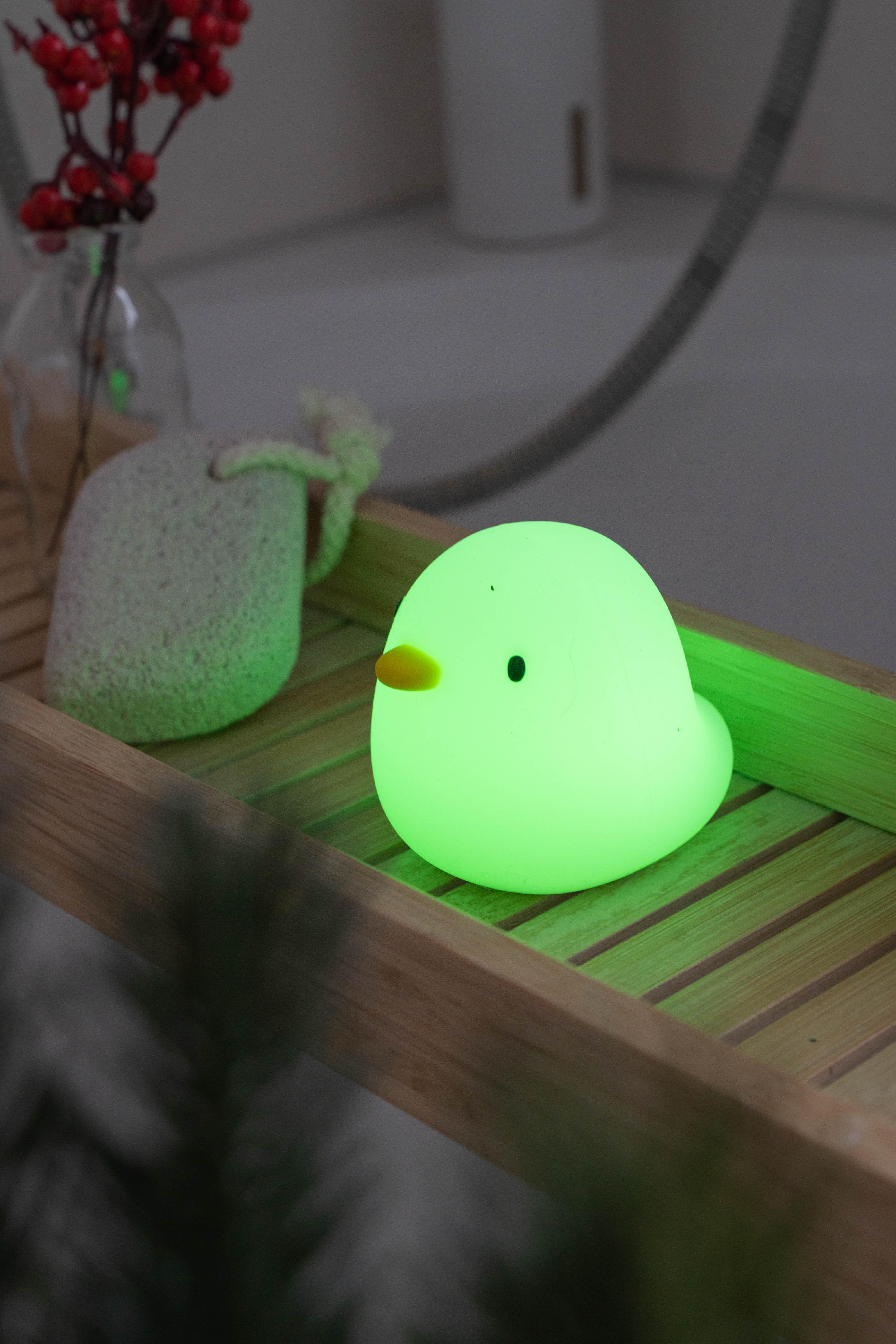 Ein grün leuchtendes, kükenförmiges Nachtlicht auf einem Holztablett.