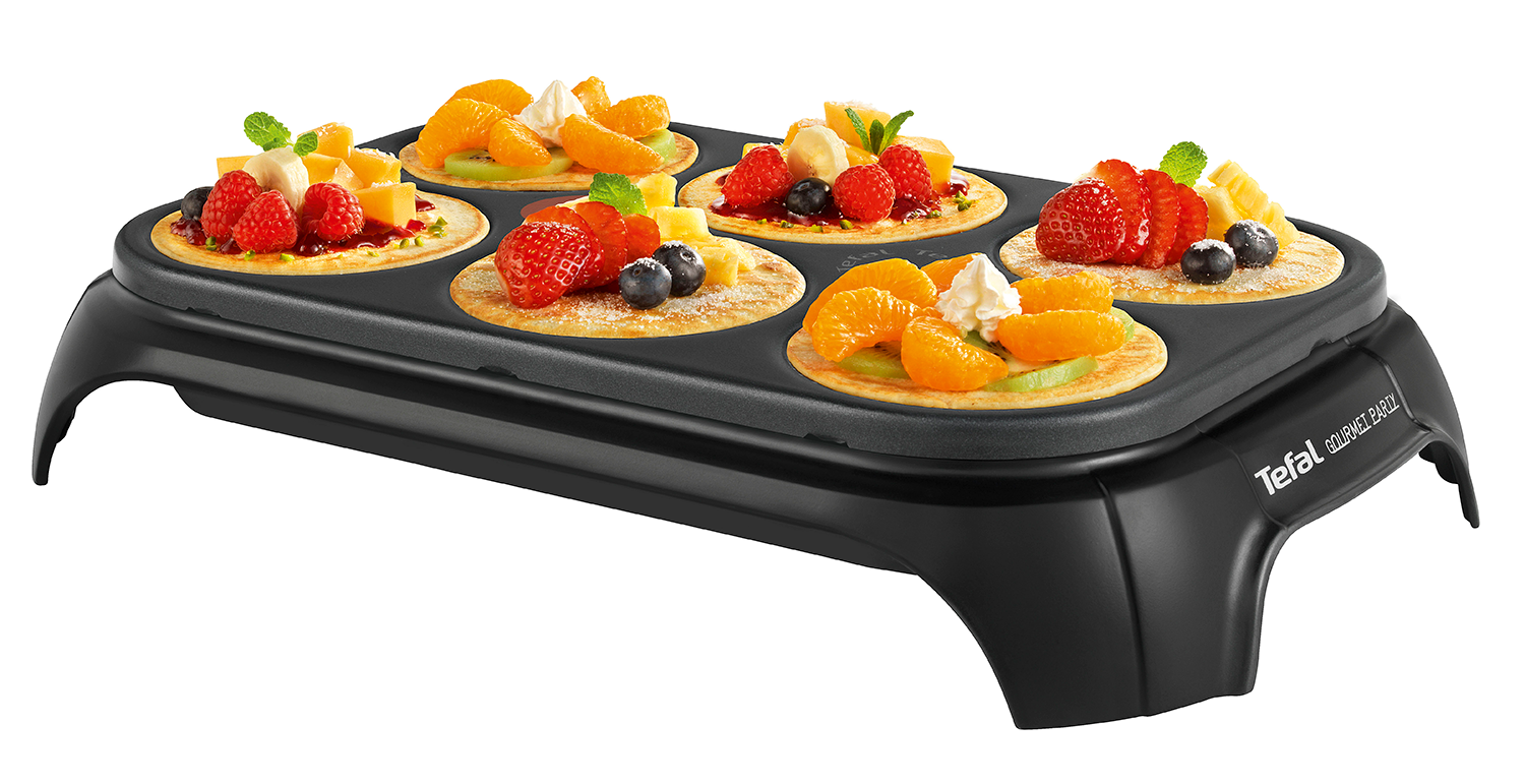 Black electric crepe maker with six crepes, each topped with fruit and cream.