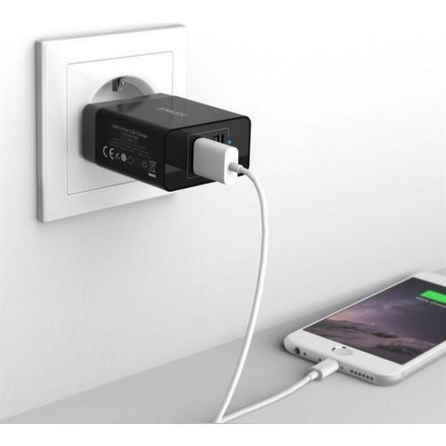 Zwarte oplader aangesloten op een wit stopcontact, een witte telefoon aan het opladen.