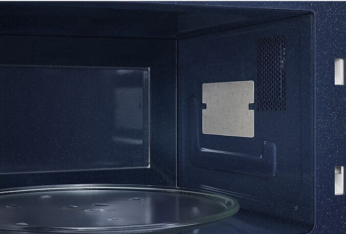 Wnętrze kuchenki mikrofalowej, ciemnoniebieskie, ze szklanym talerzem i prostokątnym elementem po prawej.