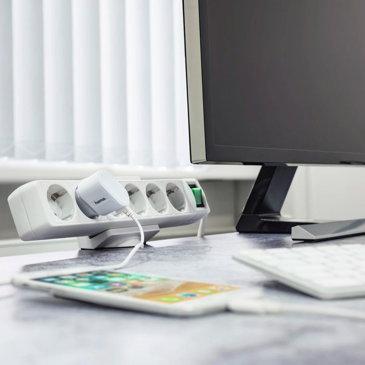 Une multiprise blanche avec un téléphone en charge, une prise et un moniteur en arrière-plan.