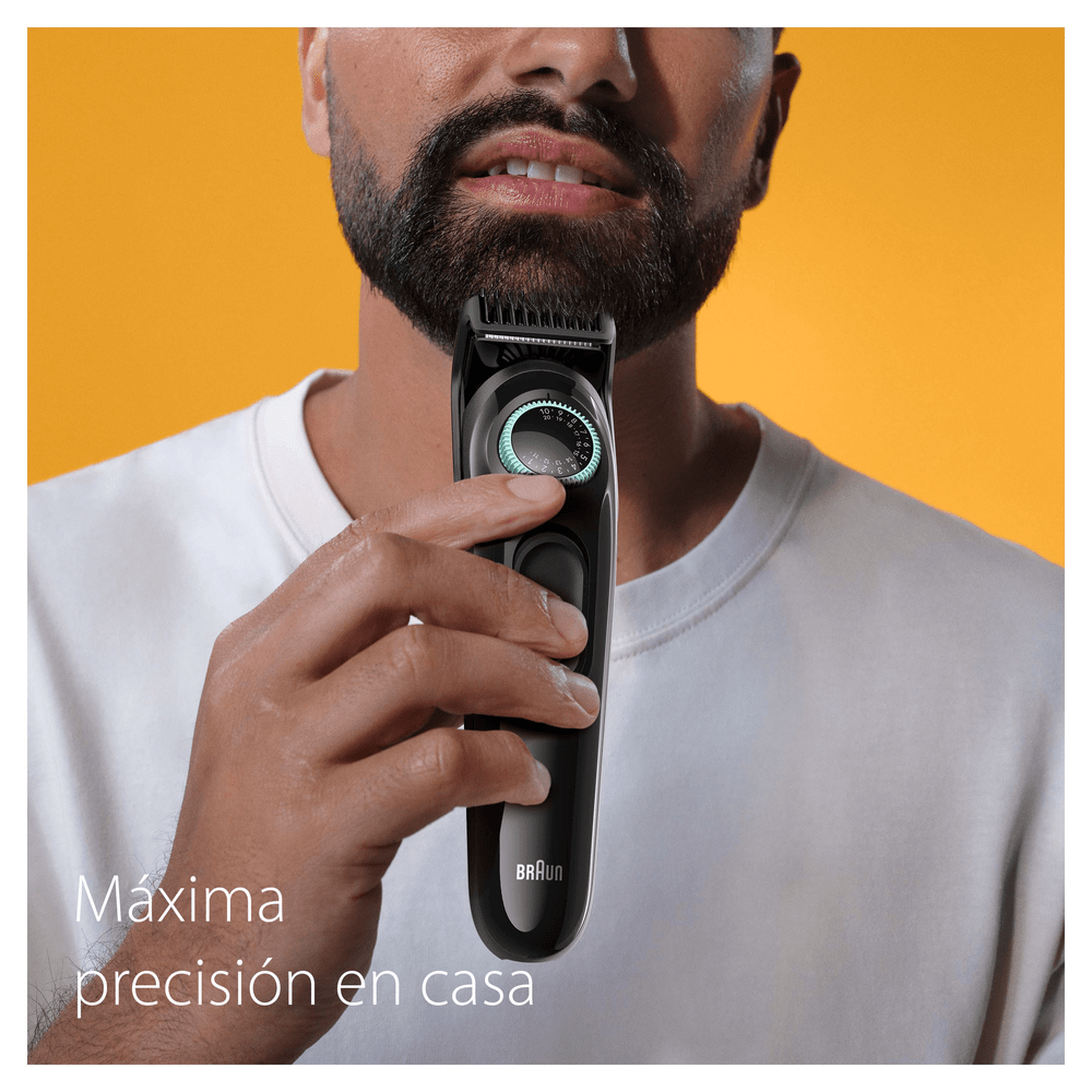 Hombre recortando su barba con una recortadora negra, con un fondo amarillo.
